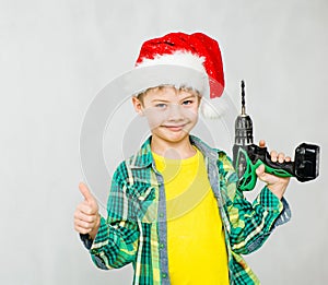 Boy in a red christmas hat with a drill showing thumbs up