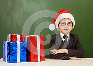 boy in red christmas hat with gift boxes near empty green blackboard