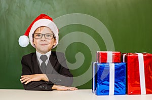 boy in red christmas hat with gift boxes near empty green blackboard