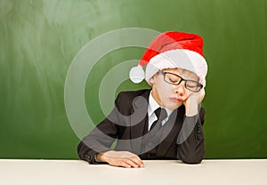 Boy in red christmas hat sleeping near empty green blackboard