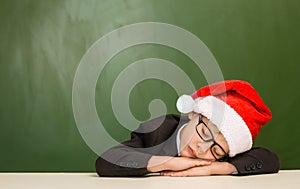 Boy in red christmas hat sleeping near empty green blackboard
