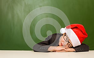 Boy in red christmas hat sleeping near empty green blackboard