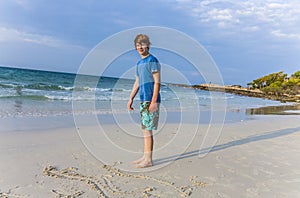 Boy with red hair is writing a message in the sandy beach