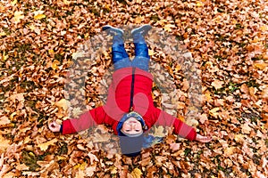 A boy in a red jacket lies on yellow maple leaves