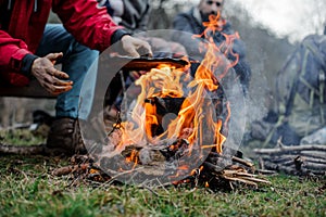 Boy in a red jacket placing a cover on the black pan standing on the bonfire
