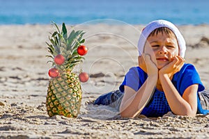 Boy in red Santa hat lying at sea beach during Christmas vacation