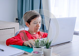A boy in red shirt focusing on study in computer, homeschool concept.