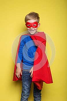 Boy in red super hero cape and mask. Superman. Studio portrait over yellow background