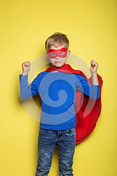 Boy in red super hero cape and mask. Superman. Studio portrait over yellow background