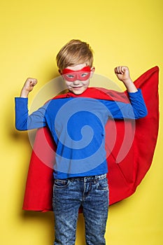 Boy in red super hero cape and mask. Superman. Studio portrait over yellow background