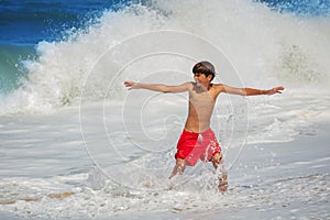 Boy, in red swim shorts with outstretched arms have fun at waves