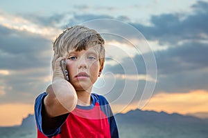 Boy in red t-shirt is sitting outdoors and talking on his mobile phone, he looks upset or scared. A teenager uses a cell