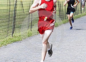 Boy in red uniform racing on gravel during a cross country race