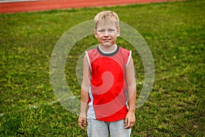 The boy in the red vest standing on green grass