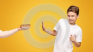 Boy Rejecting a Hotdog Offered by an Adult on a Yellow Background