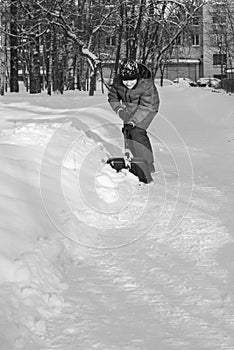 A boy removes snow with a shovel from a pedestrian path