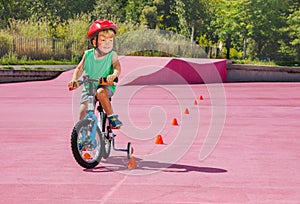 Boy ride small bicycle with learning wheels around orange cones