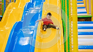 A boy rides from the children& x27;s slides on the playground in the game entertainment center. Active leisure. Childhood
