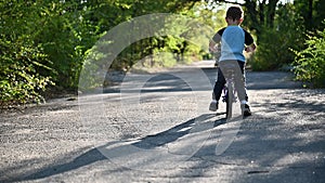 The boy rides on a runbike in the park in summer sunny weather having a good mood