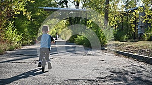 The boy rides on a runbike in the park in summer sunny weather having a good mood