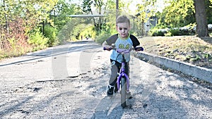 The boy rides on a runbike in the park in summer sunny weather having a good mood