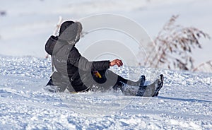 The boy rides a sled from the mountain in winter