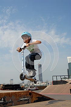 Boy rides scooter in skate park under blue sky, with available copy space.