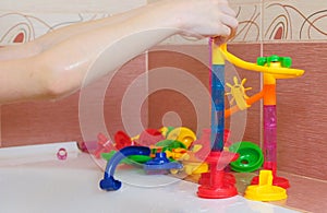 Boy rolls the ball from the plastic slide of colored designer in the bathroom. Closeup boy`s hand.