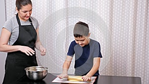 boy rolls out the dough under the supervision of a woman