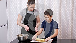 Boy rolls out dough under the supervision of a woman slow motion