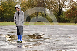 Boy in rubber blue rain boots walking in the rain