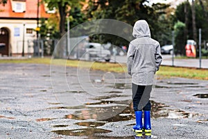 Boy in rubber blue rain boots walking in the rain