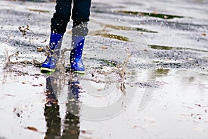 Boy in rubber blue rainboots jumping to dirty puddle photo