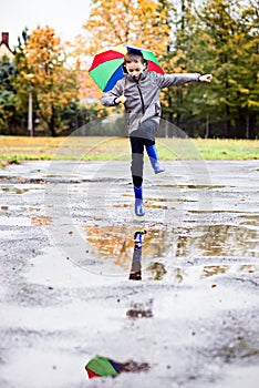 Boy in rubber blue rainboots jumping to dirty puddle