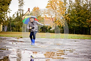 Boy in rubber blue rainboots jumping to dirty puddle