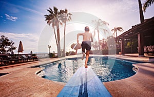 Boy run on diving board jumping to pool at sunset