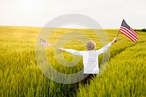 Boy runing with the american flag on the green wheat field celebrating national independence day. 4th of July concept