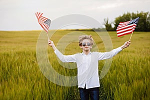 Boy runing with the american flag on the green wheat field celebrating national independence day. 4th of July concept