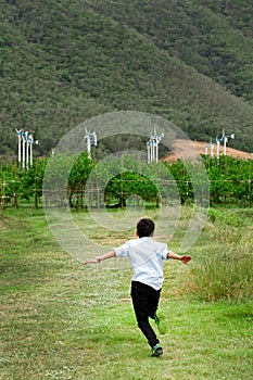 Boy running in field and wind turbines in backgroun