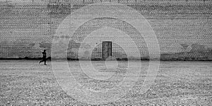 Boy running in front of wooden door on brick wall. Black and white