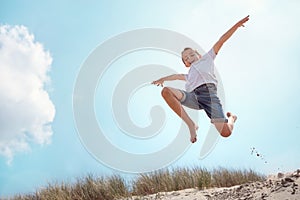 Boy running and jumping over sand dune on beach vacation