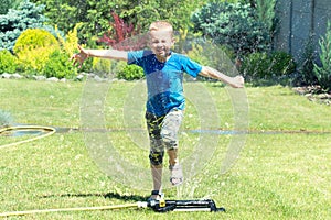 Boy running on the lawn sprinkler playing with water splashes . Summer vacation day.