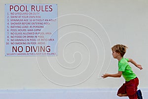 Boy running by a `Pool Rules` sign