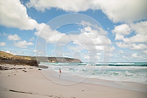 Boy running from waves on the beach with wind turbines on cliff in the background