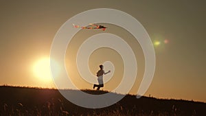 A boy runs across the field at sunset with a kite flying over his head. A chidhood dream. Kids Games