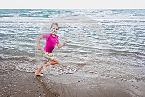A boy runs along the shore of the beach wearing a face mask during the new normality