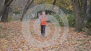 Boy runs through the fallen leaves shuffling his feet, lifting the autumn leaves to the top.