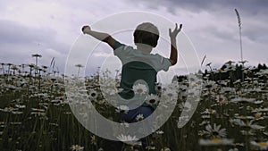 The boy runs through the meadow with flowers. CREATIVE. Rear view of a child running through a field of daisies. A child