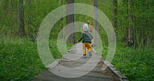 A boy runs in a Park on a wooden path in slow motion. Adventure of a boy in the forest. A 2-3 year old boy runs over a