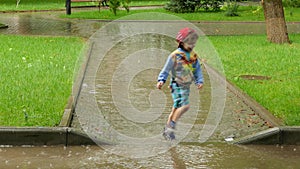 The boy runs through the puddle in the rain.